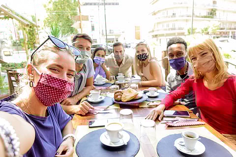 Multiracial group of friends wearing protection mask at the restaurant. Happy people celebrating toasting red wine taking a selfie with smartphone.