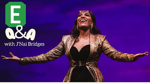 Opera singer J'Nai Bridges wearing a gold patterned blazer over a black outfit, smiling with arms outstretched against a vibrant purple background. The text on the left reads 'Q&A with J'Nai Bridges' with a green hexagonal 'E' logo above.
