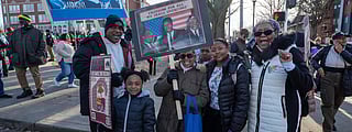 A group of Black people holding MLK-related signs pose for a photo, smiling.
