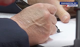A hand holding writing on paper with a large black pen.