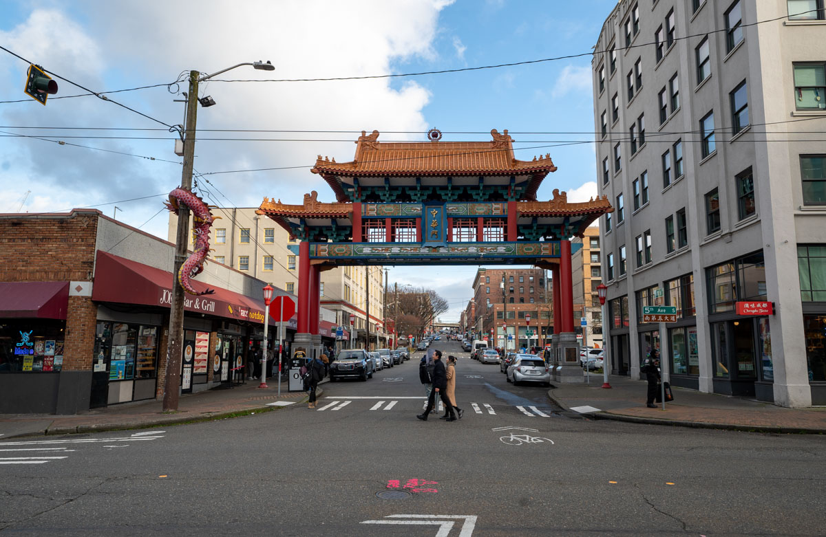 A couple walks across an urban street under a gateway with Chinese ornamentation.