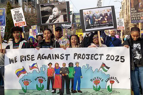 A group of young people lead the MLK Jr. Day march on Jan. 20. They're holding a large sign that reads "We Rise Against Project 2025" and a crowd is visible behind them.