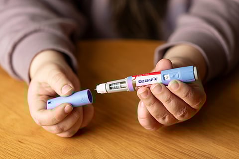 A person, with only their hands and arms visible, holds an Ozempic injectable pen.