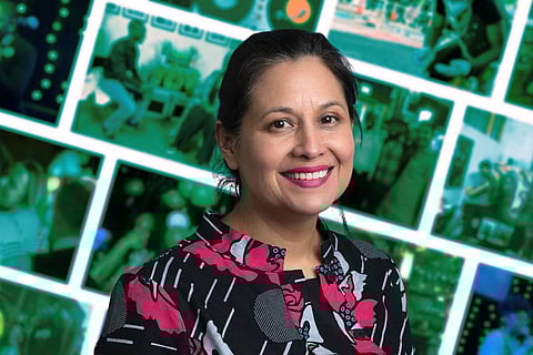 Smiling woman with dark hair tied back, wearing a black and pink patterned top, against a background featuring a collage of green-tinted images showing various scenes and people.