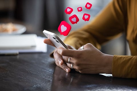 A close-up of a person's hands holding a smartphone, with multiple floating red heart icons.