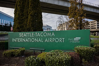 A large green sign reading "Seattle-Tacoma International Airport" with the "Port of Seattle" logo is displayed in the foreground, surrounded by neatly trimmed bushes.