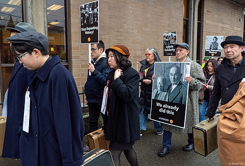 A group of people dressed in 1940s' period clothes walk while carrying signs in support of immigrants.