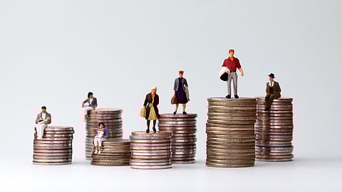 A conceptual image showing miniature figurines of people standing or sitting on stacks of coins of varying heights, symbolizing income inequality or financial disparity.