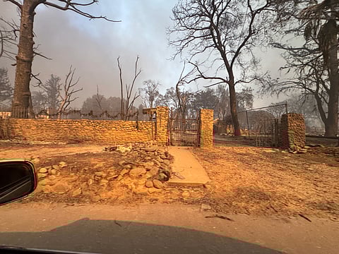 The remains of Nafasi Ferrell’s family home in Altadena, California, after the Eaton Fire tore through the neighborhood in January 2025. Burned trees and smoke surround the remains.