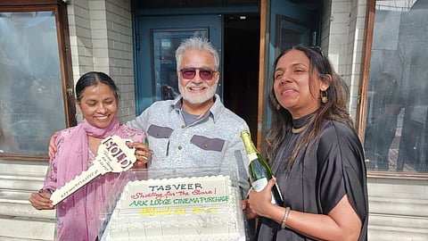 Tasveer celebrates its new acquisition of Columbia City’s Ark Lodge Cinemas. Three people stand together smiling around a cake that reads "Tasveer, Shooting for the Stars! Ark Lodge Cinema Purchase." One of them holds a large key that reads "SOLD."