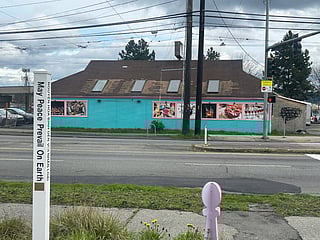 Capri Hookah Lounge photographed from across the street; in the foreground is a post that reads, vertically, "May Peace Prevail on Earth."