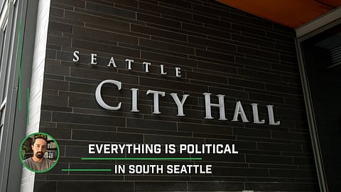 Exterior view of Seattle City Hall with large silver letters on a dark brick wall, accompanied by the caption “Everything Is Political in South Seattle” and a small circular portrait of a man in the lower left corner.