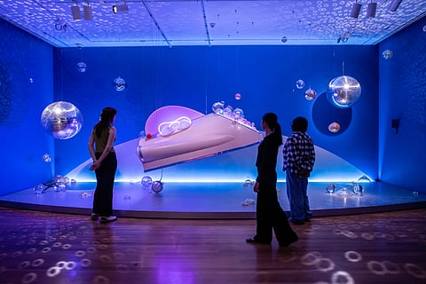 A futuristic installation at Tariqa Waters' "Venus is Missing" features disco balls, ball-barrettes, and a spaceship. A few people stand in front of the installation to view it.