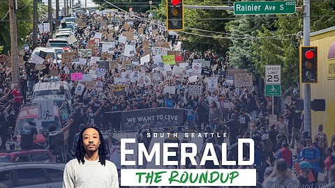 A large crowd of protesters marches down a street holding signs that say “Black Lives Matter,” “Defund the Police,” and “We Want to Live.”
