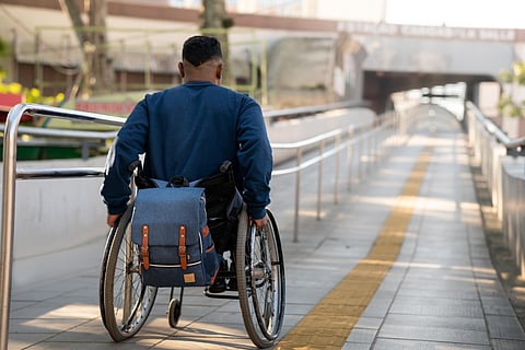 A Black-presenting person in wheelchair using accessible ramp with tactile paving and handrails.