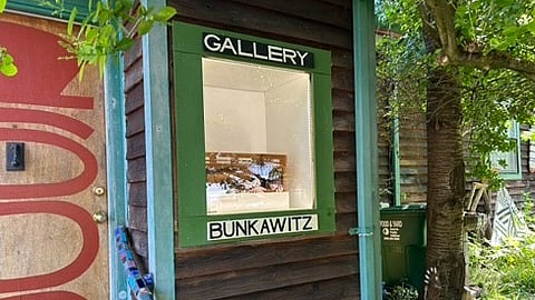 Bunkawitz Gallery display window on a rustic wood-paneled building in a garden setting.