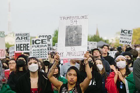 Immigration protest with woman holding “Trump’s Felonie 34, My Abuelita 0” sign, amid crowd demanding ICE abolition and immigrant rights in Seattle demonstration.
