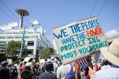 Seattle protest near the Space Needle with demonstrator holding handmade sign advocating for collective power and protection of vulnerable communities during march.