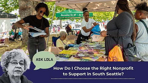 People working a booth at the 2023 Back2School Bash, overlaid with a cutout of an older Black woman labeled "Ask Lola" and the question "How Do I Choose the Right Nonprofit to Support in South Seattle?" in bold text.