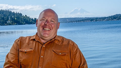 Seattle City Council candidate Jamie Fackler smiling in a burnt orange shirt by Lake Washington on a clear day.