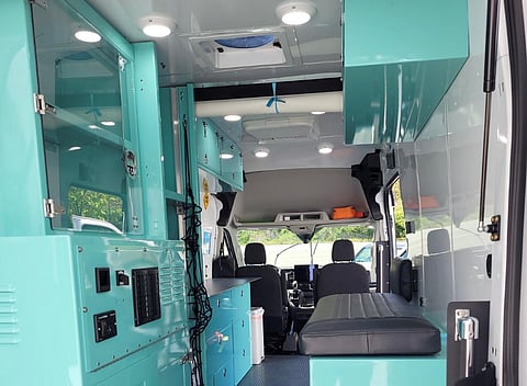 Interior view of a King County Street Medicine van, featuring teal-colored medical cabinets, seating, storage compartments, and bright overhead lighting, designed for mobile healthcare services.