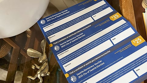 Seattle Democracy Vouchers for the 2025 City of Seattle Election, each worth $25, displayed on a table beside a small metallic rabbit figurine and household items.