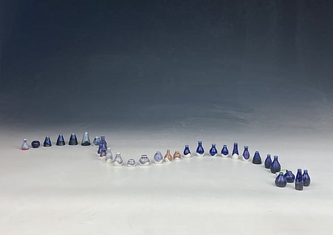 A series of small artworks in a curving line sit on a surface that shifts from white to gray.