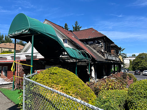 A building with a maroon roof and green awning shows signs of fire damage.