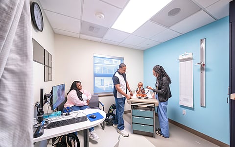 Pediatrician examines a baby sitting on a clinic exam table while parents observe during a check-up at Seattle Children’s Odessa Brown Children's Clinic.
