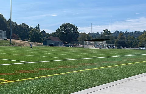 A playfield on a sunny day, with a couple of people playing sports on the field.