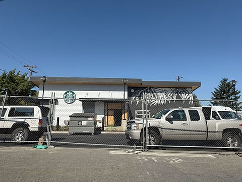 Drive-thru Starbucks under construction in Rainier Beach, Seattle, with fencing, parked trucks, and a black-and-white mural on the building’s exterior wall.
