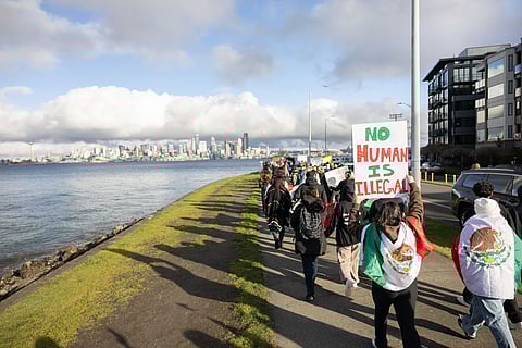 Activists march along Alki Beach to protest the U.S. Immigration and Customs Enforcement (ICE) and the Trump administration's immigration policies on Feb. 2, 2025. One holds a sign that reads "No Human Is Illegal."