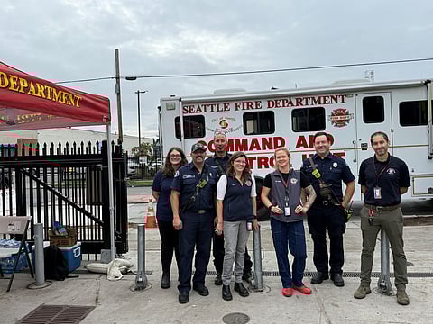 Seattle Fire Department team standing in front of a command and control unit at a community pop-up clinic, with staff and firefighters smiling under a red SFD canopy.