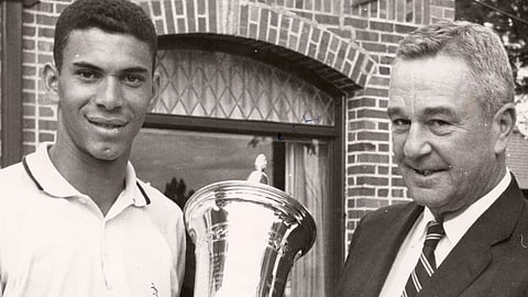 Black golfer Bill Wright smiles while holding a large trophy alongside a white official after winning the 1959 U.S. Amateur Public Links Championship.