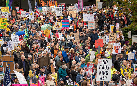 Large crowd of protesters gathered outdoors holding colorful signs with slogans like “No Faux King Way,” “Dissent is Not Disloyalty,” and “Fight Truth Decay,” opposing authoritarianism and promoting democracy under overcast skies.