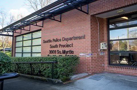 The exterior of the Seattle Police Department South Precinct, labeled with its address in lettering on the side of the building behind some bushes.