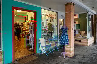 Exterior of Andaluz with turqouise storefront, outdoor display table, and a floral dress on a mannequin as shoppers browse inside.