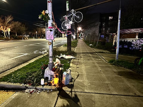 Ghost bike with flowers and lit candles tied to a utility pole at a Beacon Hill street corner in Seattle, memorializing a cyclist killed in a hit-and-run crash at night.