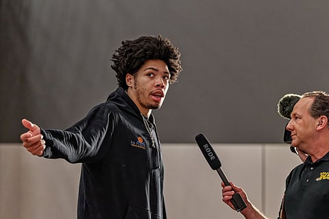Tyran Stokes, high school basketball senior, gestures while being interviewed by KING-5 reporter Chris Egan before a game, wearing a black hoodie inside a gym.