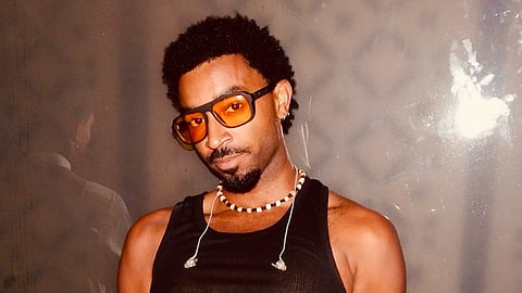Harrison Clark, South Seattle artist, wearing a black tank top and amber glasses, posing against a neutral backdrop with a calm, confident expression.