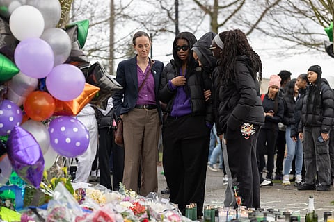 Seattle Mayor Katie Wilson stands with students and community members at a Rainier Beach bus stop memorial, surrounded by candles, flowers, and purple balloons honoring two teens killed in a shooting.