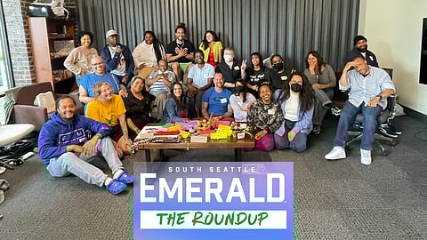 A group of people gathered around a coffee table pose for a photo, many of them smiling.