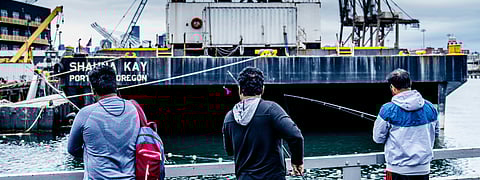 People in a small boat pull a net from the water beside railroad tracks and freight cars.