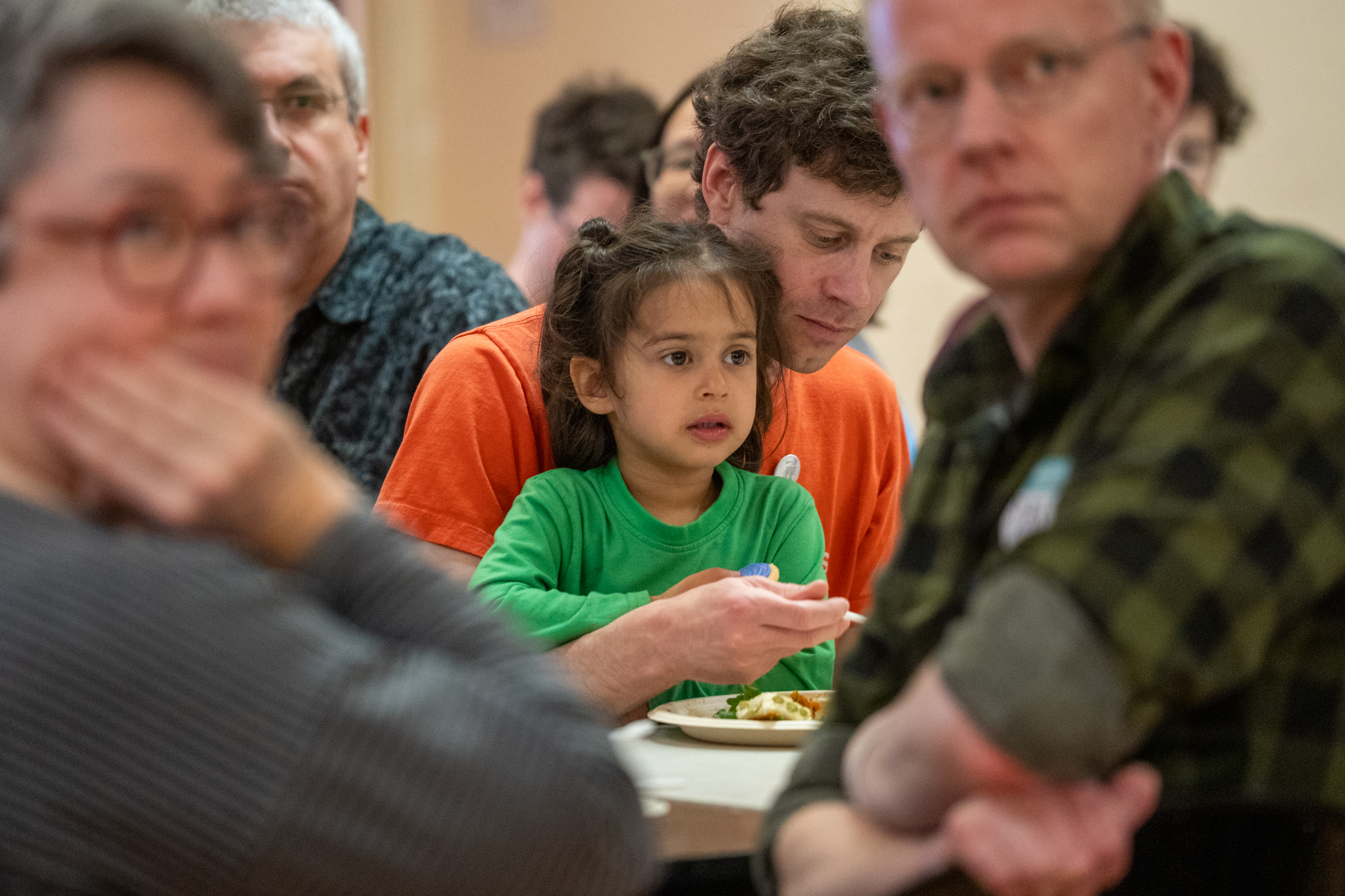 A 3-year-old sits in her father's lap, as both participate in a monthly potluck hosted by the Columbia City Neighbors Club. This potluck served as the starting point for a yearlong, nationwide “Interdependence Relay,” designed to counter isolation by bringing neighbors together.