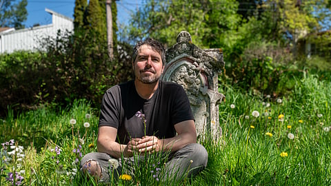 J.J. Gerber sits in tall grass beside a historic gravestone at Comet Lodge Cemetery.