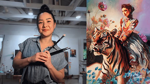 Portrait of Karen Chang holding paintbrushes beside a vibrant fantasy painting of a woman riding a tiger surrounded by flowers.