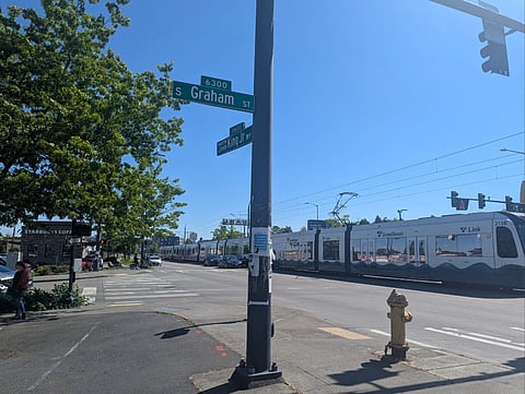 A light rail train passes through the future site of the Graham Street Station. Street signs read "Martin Luther King Jr. Wy" and "Graham St."