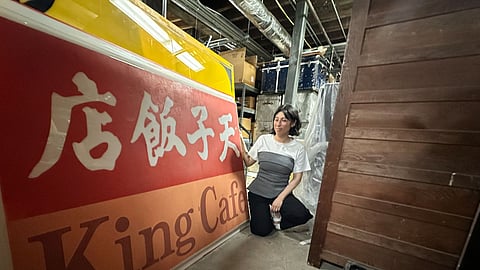 Chrissy Shimizu beside a historic King Cafe sign in the Wing Luke Museum collections basement.
