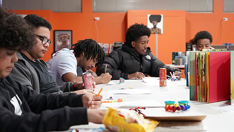 Young authors write at a table with books and art supplies