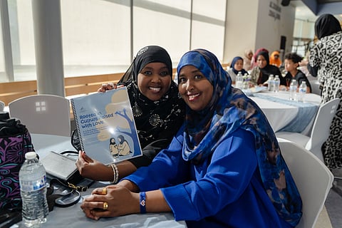 Nas Abdi and Fadumo Abdi smile and hold up a print copy of the toolkit.